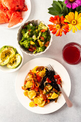 A filling breakfast of black rice with stewed tomatoes, zucchini, peppers, and onions, accompanied by a fresh salad of tomatoes, broccoli, radish, and avocado