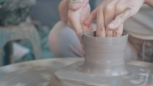 A potter skillfully shapes clay on a spinning wheel, demonstrating the art of pottery making. The hands are covered in clay, showcasing the tactile and creative process involved in crafting unique cer