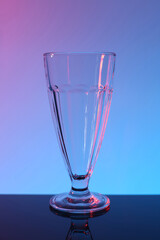 One empty glass on table against color background