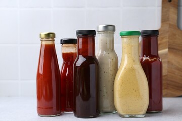 Tasty sauces in glass bottles on white table, closeup
