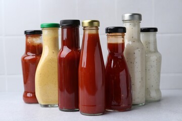 Tasty sauces in glass bottles on white table, closeup