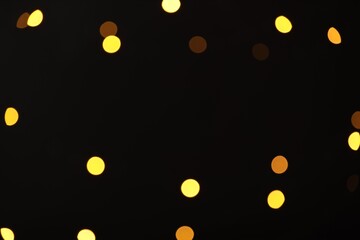 Blurred view of golden lights on black background, bokeh effect