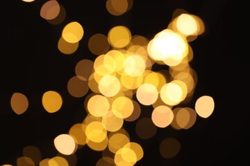 Blurred view of golden lights on black background, bokeh effect