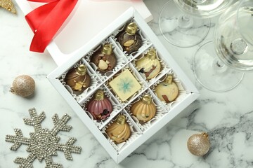 Box with tasty sweets in shape of baubles, wine and Christmas decor on white marble background, flat lay