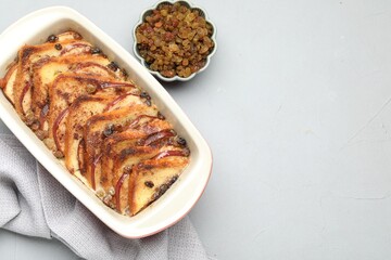 Delicious bread pudding in baking dish and raisins on light gray table, flat lay. Space for text