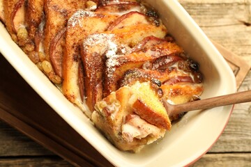 Taking tasty bread pudding from baking dish at wooden table, top view