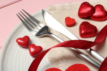 Romantic place setting for Valentine's day. Cutlery, napkin, plate and decorative hearts on pink wooden table, closeup