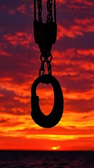 A dramatic perspective of a crane hook silhouetted against the fiery hues of sunset.