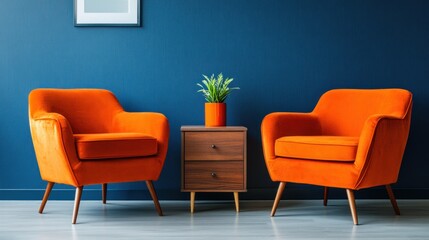 Two orange armchairs face each other with a small wooden side table and plant between them against a dark blue wall.