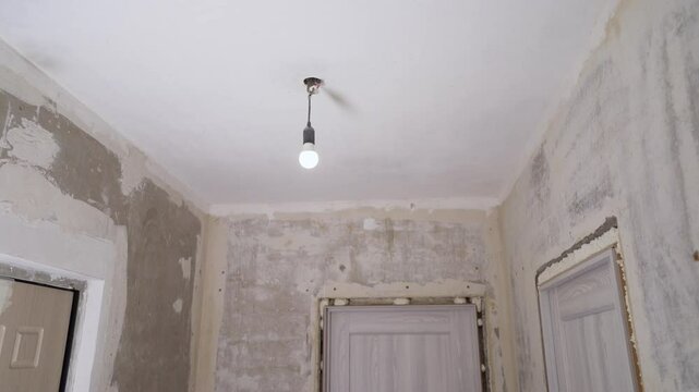 Single light bulb swings gently, illuminating a room undergoing renovation, with bare walls and doorways awaiting finishing touches