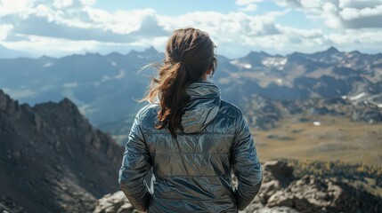 Naklejka premium A young woman in a metallic jacket standing on a mountain trail, her back to the camera as she gazes at the horizon.