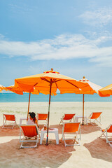Woman sit on the orange umbrella chair set on the beach with blue sky.