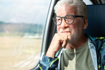 Portrait of senior smiling man with eyeglasses enjoying the train ride sitting in passenger seat by...