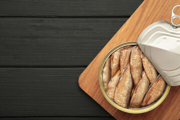 Canned smoked sprat fish in oil in jar on black wooden background. Top view.