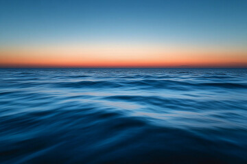 Obraz premium Sunset over calm ocean waters creates a serene atmosphere with vibrant colors on the horizon
