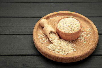Raw sesame seeds in wooden bowl and spoon on black background.