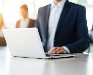 A man in a suit is sitting at a desk with a laptop open in front of him