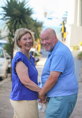 Naklejka premium happy senior couple smiling walking down the street holding hands on summer day