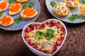 Salad with chicken and pineapples in a heart-shaped salad bowl next to tartlets and sandwiches