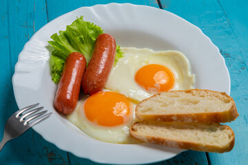Breakfast fried eggs with sausages, crispy white bread and greens, on a blue table. Horizontal photo.