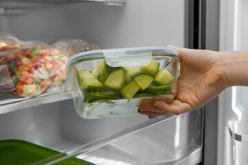 Woman taking glass container with frozen chopped zucchini from refrigerator, closeup