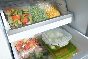 Plastic bags and glass containers with different frozen vegetables in refrigerator