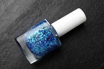 Glitter nail polish in bottle on dark textured table, top view