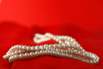 Beautiful pearl necklace on red silk, closeup