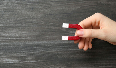 Woman with horseshoe magnet on wooden background, top view. Space for text