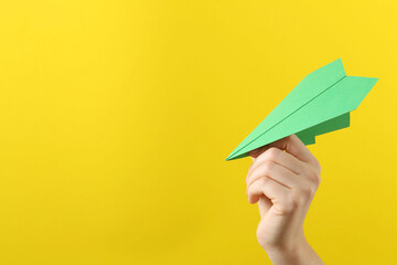 Woman with green paper plane on yellow background, closeup. Space for text