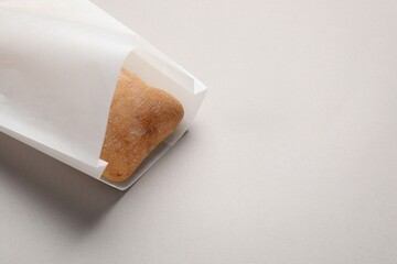 Paper bag with fresh ciabatta on beige background, closeup. Space for text