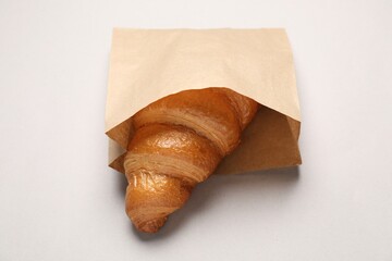 Paper bag with fresh croissant on beige background, closeup