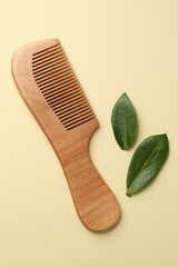 Wooden comb and leaves on beige background, flat lay