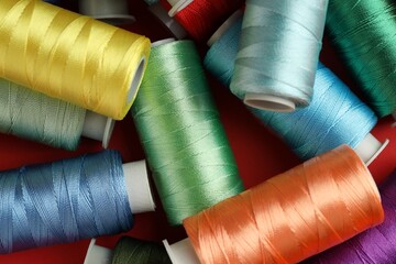 Different spools of sewing threads on red background, top view