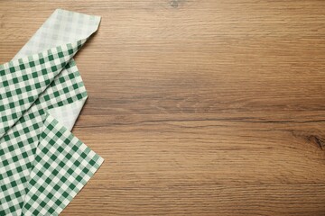 Green checkered tablecloth on wooden background, top view. Space for text