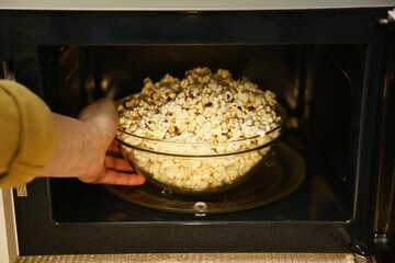 Woman taking bowl with popcorn out of microwave oven, closeup