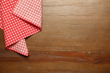 Obraz premium Red checkered tablecloth on wooden background, top view. Space for text