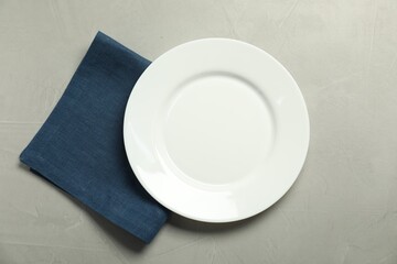 Blue napkin and empty plate on grey table, top view