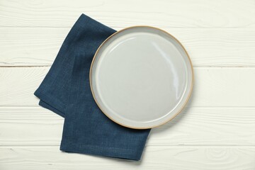 Blue napkin and empty plate on white wooden table, top view