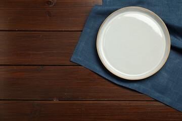 Blue napkin and empty plate on wooden table, top view. Space for text