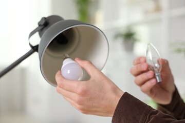 Man changing incandescent light bulb for fluorescent one in lamp at home, closeup