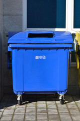 A blue paper recycling container in front of a building
