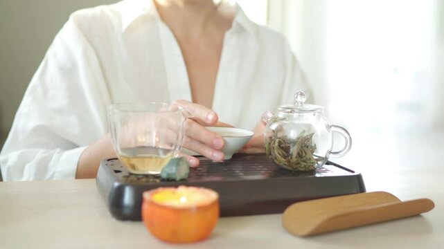 Female enjoying aged white tea taste and aroma from porcelain teacup exuding warmth and tranquility. Elegant setup with teapot and glass pitcher enhances an intimate, soothing tea ceremony experience