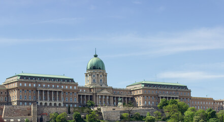 Buda Castle with its iconic dome and historic architecture surrounded by greenery under a clear blue sky in Budapest, Hungary.
