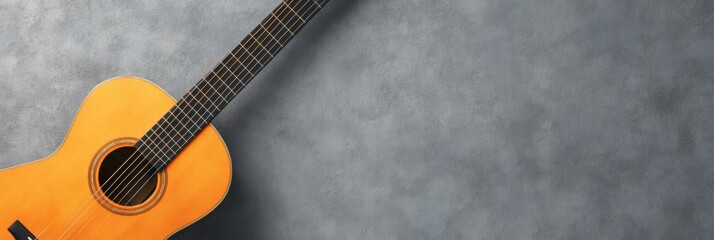 Obraz premium Classic orange wooden acoustic guitar lying on gray textured background with copy space, creating a simple yet evocative scene of musical potential