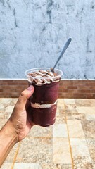 hand holding glass with açaí, nest milk and Nutella. Açaí is a very common palm tree in the Amazon region that produces a purple-colored fruit.