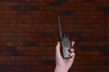 Woman with walkie talkie against brick wall, closeup. Space for text