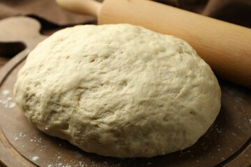 Fresh dough and rolling pin on table, closeup