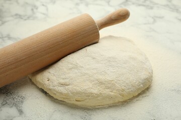 Fresh dough and rolling pin on white marble table, closeup