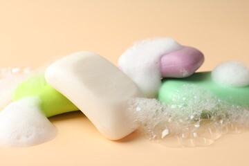 Soap bars with foam on beige background, closeup